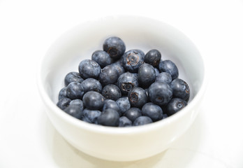 Fresh blue berries in the white bowl on the white stone table.