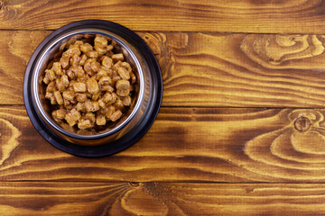 Canned food for cats or dogs in metal bowl on wooden floor. Top view