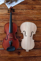 The wooden violin and bow put beside unfinished violin,on wooden timber board,blurry light around
