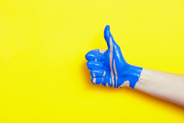 female hand showing sign thumb up with paint flowing down on a colored background. creative idea,...