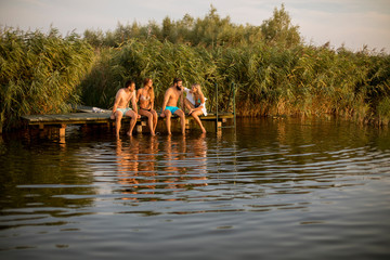 Portrait of happy young friends sitting on pier at the lake