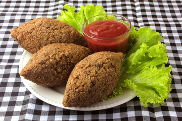 kibbeh fried with tomato sauce on a plate, on table lined with checkered tablecloth