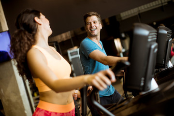 Young woman and man on elliptical stepper trainer exercising in gym