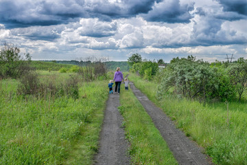 Fototapeta na wymiar Woman and children walk on road under dark clouds
