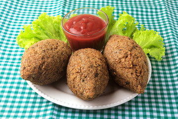kibbeh fried with tomato sauce on a plate, on table lined with checkered tablecloth