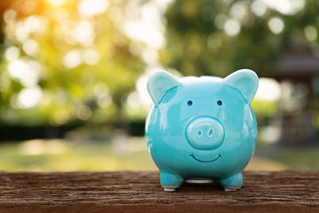 Blue piggy bank on wooden table over blurred green bokeh background. Saving money concept - obrazy, fototapety, plakaty