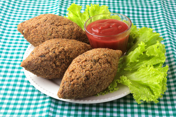 kibbeh fried with tomato sauce on a plate, on table lined with checkered tablecloth
