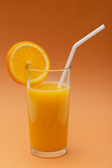 a glass of orange juice on an orange background with a straw and a slice of orange