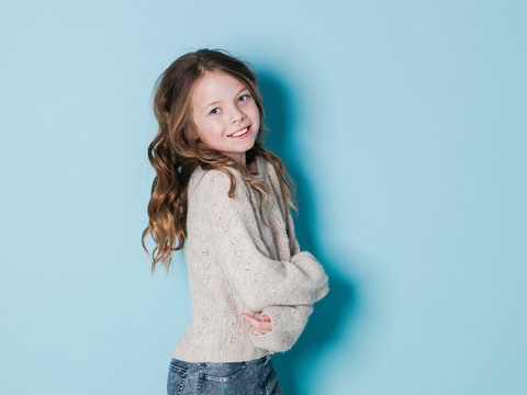 pretty and cool 9 year old girl with brown wool sweater posing in front of blue background
