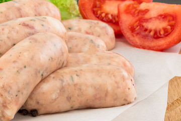 Fresh raw sausage with lettuce and tomato on the wooden background