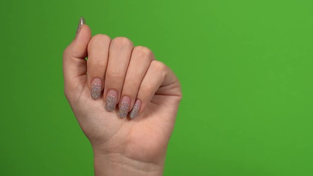 Closeup view of beautiful female hands with old silver sparkling manicure isolated on green background. Woman needs correction. 4k video footage.