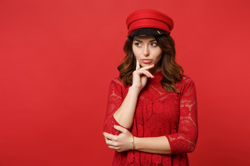 Portrait of thinkful young woman in lace dress, cap looking aside, put hand prop up on chin isolated on bright red background in studio. People sincere emotions, lifestyle concept. Mock up copy space.