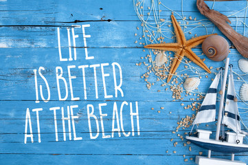 Blue wooden board with maritime decoration and life is better at the beach