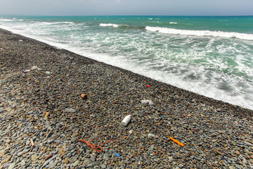 Beautiful unspoiled dark pebble stones beach with garbage, mostly plastic, washed out. Ocean littering concept.