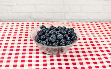 Small glass bowl with blueberries on red gingham patter tablecloth