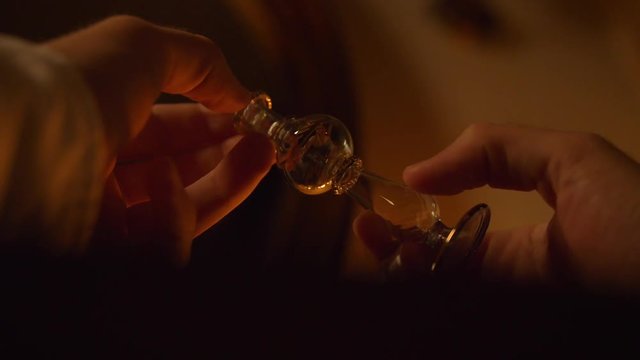 Room. Twilight. Warm colors, the light from the candles. A man turns a glass, curved vial in his hands. Then opens it, removing the cap with the pipette on the end. Fabulous, mystical theme.