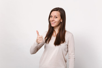 Fototapeta premium Portrait of smiling pretty young woman in light clothes looking camera, showing thumb up isolated on white wall background in studio. People sincere emotions, lifestyle concept. Mock up copy space.