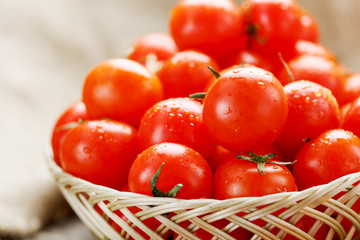 Small red tomatoes in a wicker basket on an old wooden table. Ripe and juicy cherry