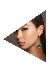 Cropped side half-turn geometric portrait of Korean woman with black flicks. The girl is wearing long earrings with round emerald pendant inside, looking at camera behind triangle-shaped foreground.