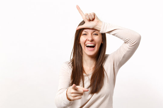 Laughing young woman in light clothes showing looser gesture pointing index finger on camera isolated on white wall background in studio. People sincere emotions lifestyle concept. Mock up copy space.