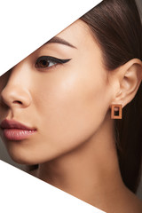 Cropped side half-turn geometric portrait of Korean girl with plush lips and black flicks. The lady is wearing a brown rectangle-shaped earring, looking directly behind triangle-shaped foreground.