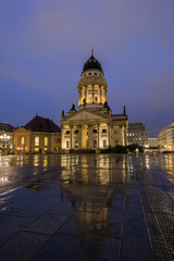 Illuminated Französischer Dom (French Cathedral) and its reflection at the wet Gendarmenmarkt Square in Berlin, Germany, in the evening.