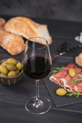 Glass of red wine with slices of cured ham or Spanish jamon serrano or Italian prosciutto crudo, bread, green olives and arugula