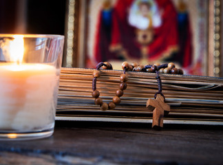 The time for prayer. Wooden Rosary on an ancient prayer book. Icon of the Mother of God and Jesus. Lighted candle