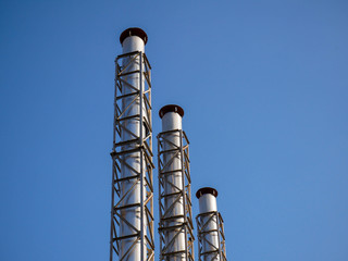 Three industrial chimneys close up shot, perfect blue sky background.