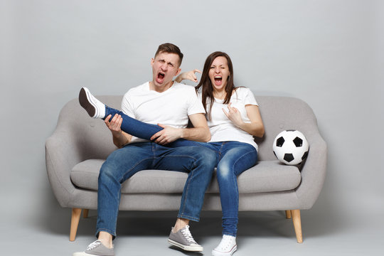 Crazy screaming couple woman man football fans cheer up support favorite team with soccer ball hold leg like guitar, showing horns up gesture isolated on grey background. Sport family leisure concept.