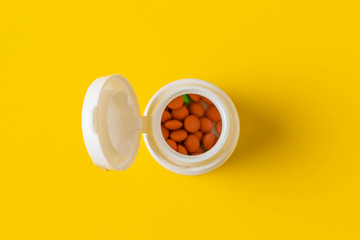 medical pills scattered from a white tube on a yellow background