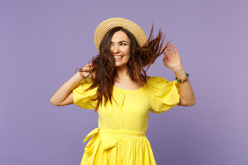 Pretty young woman in yellow dress, summer hat spreading hands with fluttering hair, looking aside isolated on pastel violet background. People sincere emotions lifestyle concept. Mock up copy space.