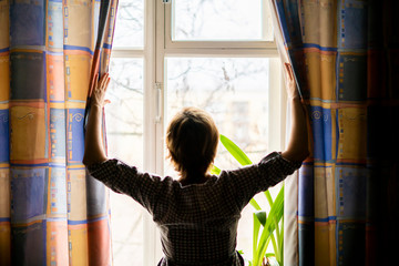woman opens the curtains and looks out the window