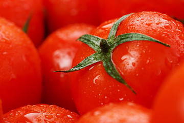 Lots of fresh ripe tomatoes with drops of dew. Close-up background with texture of red hearts with green tails. Fresh cherry tomatoes with green leaves. Background red tomatoes © Alexander