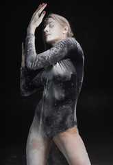 Beautiful slim girl wearing a black gymnastic bodysuit covered with white powder talcum dust jumps...