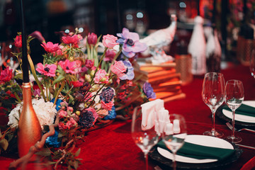 Table wedding decor in red and black tones. Pink, blue and red flowers bouquet and candles in bottles.