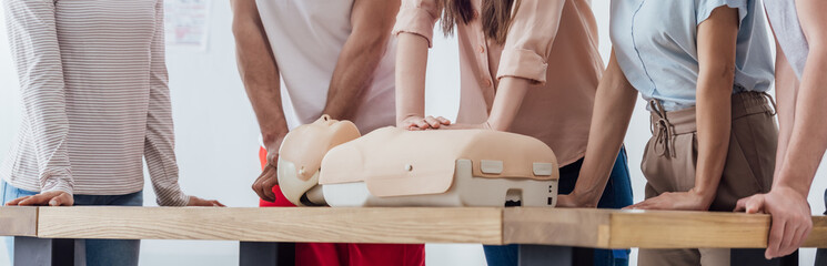 panoramic shot of group of people performing cpr on dummy during first aid training