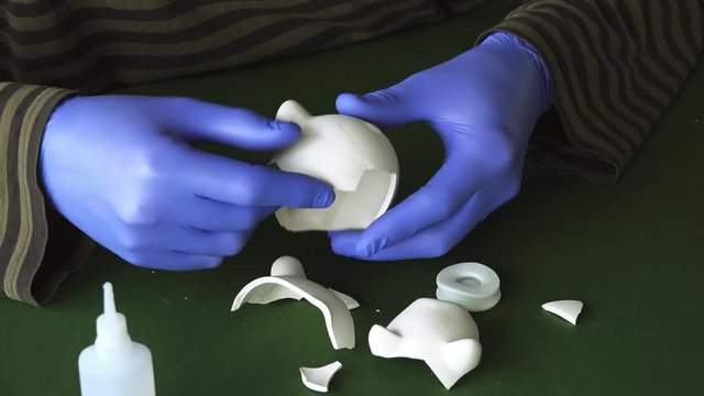 Restoring broken piggy coin bank, man using superglue to reattach pieces