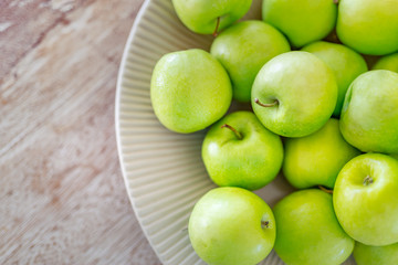 Fresh green apples in bowl on wooden background