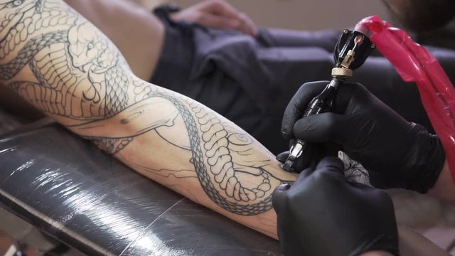 A man makes a tattoo on his hand in black ink.