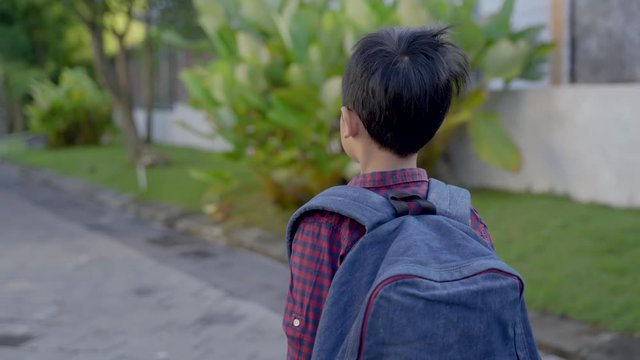 asian boy student with backpack and book standing in front of his house ready to walk to school in the morning