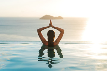 Fototapeta girl in the pool at sunset doing yoga with a view of the mountains and the sea obraz