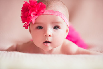 Funny baby girl wearing headband with flower lying in bed close up. Looking at camera. Childhood.