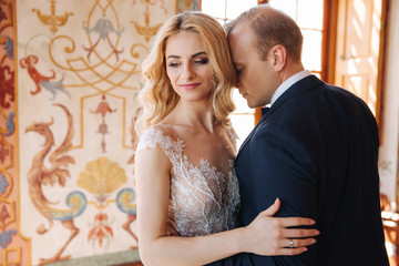 Beautiful couple in wedding dress stand in museum. They look to each other