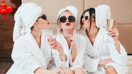 Rolgordijnen Viering feest in de spa. Vrienden gefeliciteerd. Jonge vrouwen met champagne. Zonnebril, badjassen en tulbanden op. © golubovy