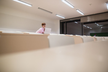 Pretty young college student/teacher with notebook/ laptop studying in modern study room during the lesson, education concept