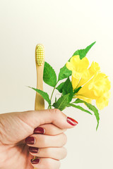 Zero-waste, biodegradable bamboo toothbrush with a yellow flower in a hand