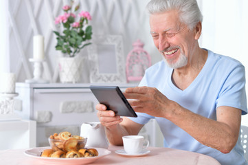 senior man using tablet while drinking tea