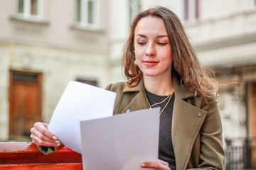 Portrait of a pretty young business lady working on a bench on the street. Papers, telephone conversations.