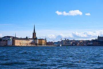 Fototapeta na wymiar Old city of Stockholm with waves on blue water under the blue cloudy sky in sunshine.